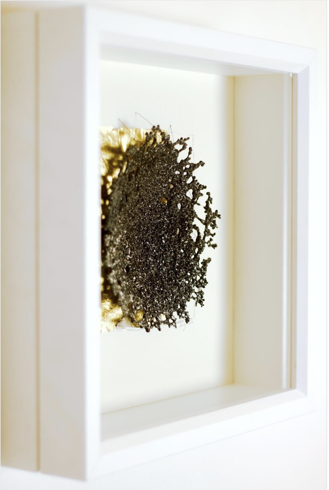 Ein schwarzes, schalenförmiges Glasobjekt auf einem Blatt Blattgold in einem Bilderrahmen